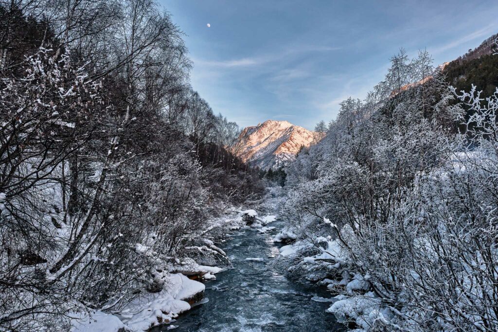 Beautiful winter landscape. A mountain river running in a snow-covered forest on sunset. Elbrus region, Russia.