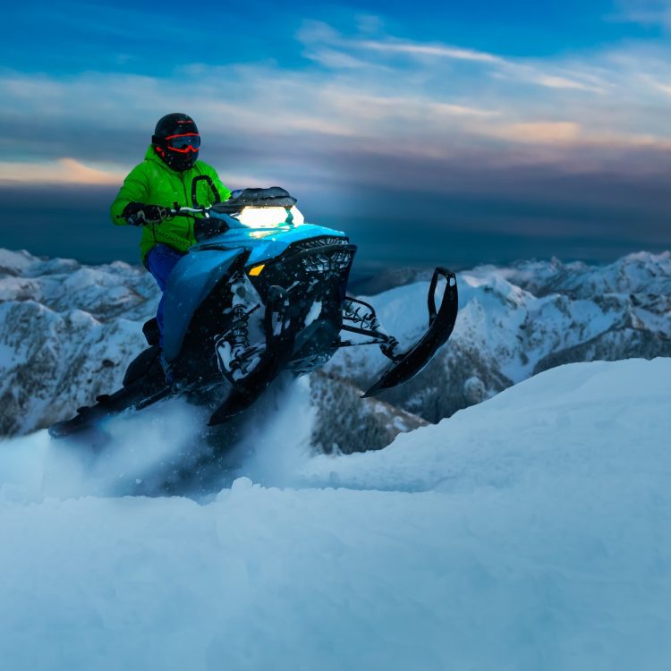 Adventurous Man Riding a Snowmobile in white snow during a colorful sunset