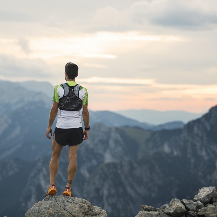 mountain running man standing on trail looking at sunset